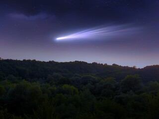 Comet in the night sky over green hills. Bright tail of a comet in the starry sky. Celestial body, astrophotography.