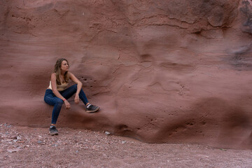 Young woman sitting against a red sandstone wall in a desert canyon