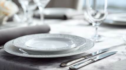Formal table setting with decorative plates and silver cutlery on a silver tablecloth