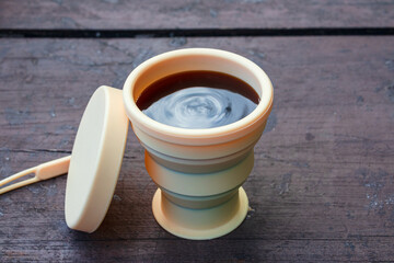 Silicone folding cup with coffee on a wooden table. Reusable tableware for travel and picnics