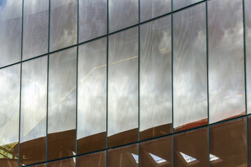 Close-up of a modern glass facade reflecting the cloudy sky and surrounding architecture