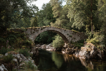 Fototapeta premium Classic stone bridge crossing a calm river, surrounded by lush greenery