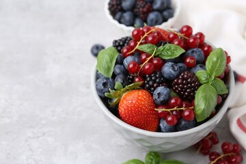 Different ripe berries and basil leaves in bowls on light grey textured table, closeup. Space for text