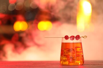 Glass of alcoholic cocktail with garnish on table against blurred background with smoke, space for text. Bokeh effect