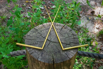 Dowsing with metal indicator L rods is a modern tool of a dowser. Two dowsing rods for the radiesthesia technique, lie on the stump of an old tree. An ancient method, not scientifically proven