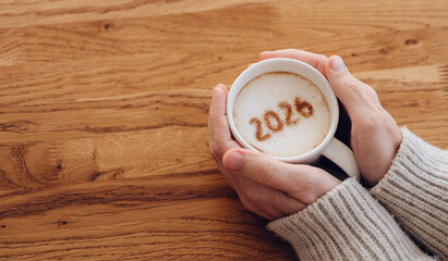 Woman in warm sweater enjoying coffee with 2026 on foam
