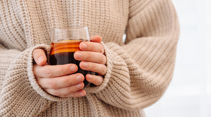 Young woman in cozy sweater holding hot mulled wine glass