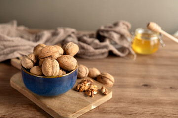 Whole walnuts in a blue ceramic bowl placed on a wooden board with honey in the background.