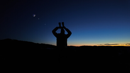 Amateur astronomer looking at the evening skies, observing planets, stars, Moon and other celestial objects with binoculars.