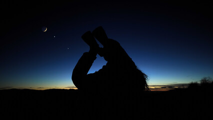 Amateur astronomer looking at the evening skies, observing planets, stars, Moon and other celestial objects with binoculars.