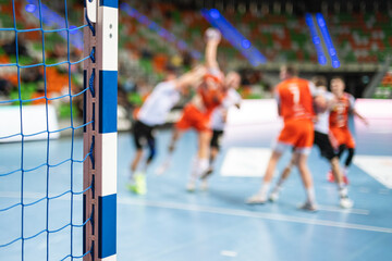 Detail of handball goal post with net and players in the background.