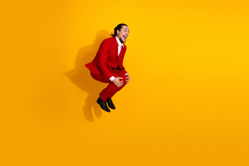 Jumping in a bold red suit man defies gravity on a bright yellow backdrop delivering playful energy fashion flair and confident charisma