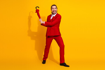 Funny showman in a bold red suit with umbrella strikes a playful pose against a bright yellow backdrop for a stylish fashion moment