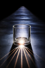 Empty glass radiating bright light beams illuminating a dark path