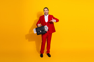 Funny flamboyant businessman in red suit drops cash from a briefcase against a vibrant yellow background at a stylish photoshoot