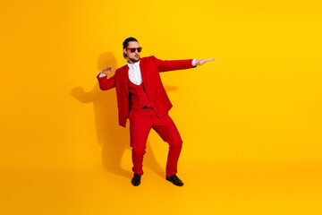 funny stylish business man dances in bold red suit against bright yellow backdrop creating a...