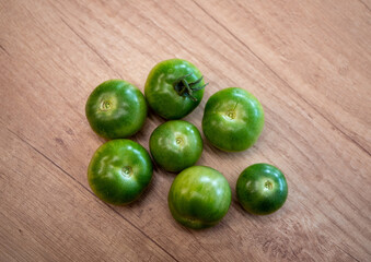 Fresh green and unripe tomatoes in a blue bowl on a wooden table. Perfect for pickling, chutney, fried green tomatoes, or to let them ripen naturally.