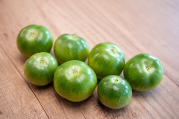 Fresh green and unripe tomatoes in a blue bowl on a wooden table. Perfect for pickling, chutney, fried green tomatoes, or to let them ripen naturally.