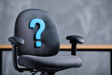 Close-up of an empty office chair with a large blue question mark on the back