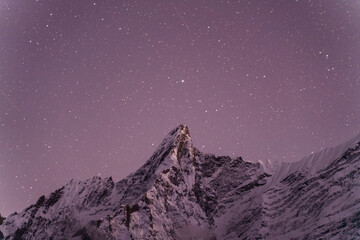 Stars dance above a snow-capped mountain peak