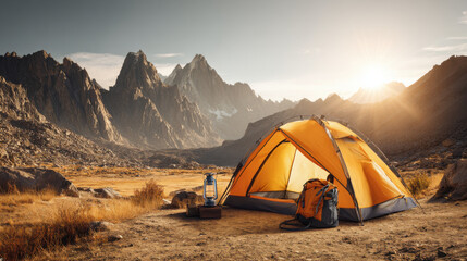 Camping adventure in mountains with tent and backpack under the sunset. Vibrant image capturing a camping scene with orange tent, backpack, and lantern set against majestic mountains during sunset