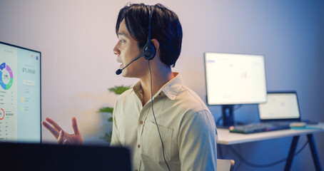 Asian businessman call center agent with headset working at night in a modern office, using computer to help customers — IT support, clear communication and professional service.