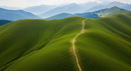 Winding dirt path ascends lush green mountain slopes under a hazy sky