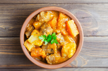 Goulash stew of stewed veal and vegetables with a feather in a ceramic bowl on a wooden background. Traditional Hungarian cuisine concept. Horizontal orientation. Selective focus. Top view.