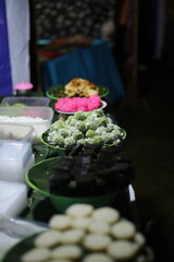 A close-up shot of stacked plates showcases a variety of Indonesian sweet snacks in the form of market snacks called Klepon.