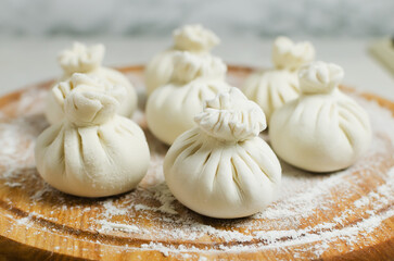 Raw khinkali on a cutting board with flour on a round cutting board on the table. Concept of traditional Georgian cuisine. Horizontal orientation. Selective focus.