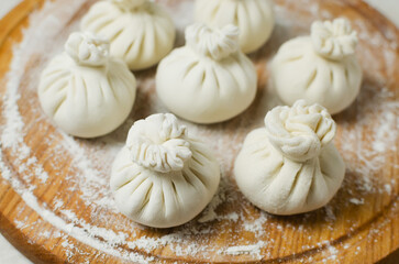 Raw khinkali on a round cutting board on the table. Concept of traditional Georgian cuisine. Horizontal orientation. Selective focus.