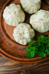 Boiled khinkali with a bunch of parsley on a ceramic plate. Rustic style. Concept of traditional Georgian cuisine. Vertical orientation. Selective focus. Top view