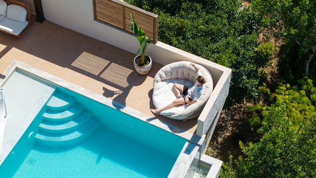 Serene Escape: A person unwinds on a chic lounger beside a refreshing pool, embracing the tranquility of a bright sunny day. 
