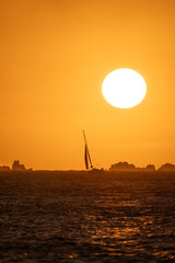 A sailboat in a golden-hour sunset with a few rocks in the background	