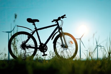 Fototapeta premium Silhouette of a mountain bike in grassy field with windmills and setting sun
