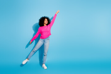 Fototapeta premium Young woman in vibrant pink sweater posing joyfully against a blue background, celebrating trendy fashion with a casual style