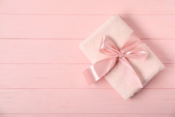 Fresh terry towel with bow on pink wooden background, top view. Space for text