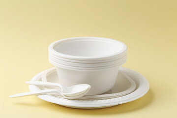 Set of disposable plastic tableware on pale yellow background, closeup