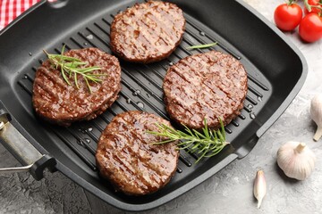 Pan with grilled patties, tomatoes and spices on grey table, closeup