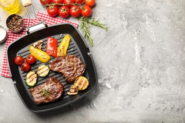 Pan with grilled beef steaks, mushrooms, vegetables and spices on grey textured table, flat lay. Space for text