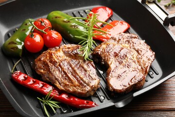 Pan with grilled beef steaks, rosemary and vegetables on wooden table, closeup