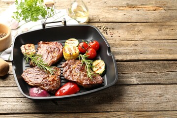 Pan with grilled beef steaks, rosemary and vegetables on wooden table, closeup. Space for text