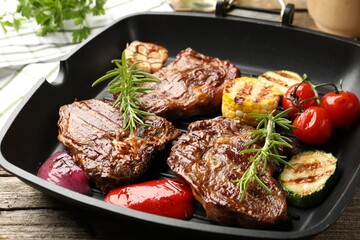Pan with grilled beef steaks, rosemary and vegetables on wooden table, closeup