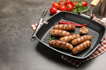 Pan with grilled sausages, spices and tomatoes on gray textured table, closeup. Space for text