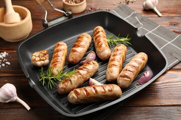 Pan with grilled sausages and spices on wooden table