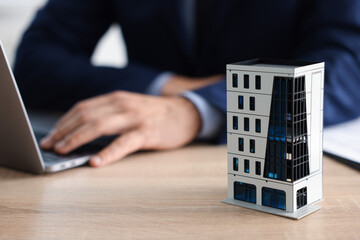 Real estate agent working with laptop at wooden table, focus on apartment building model