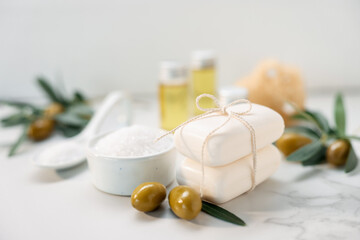 Natural soap bars, olives and sea salt on white marble table, closeup