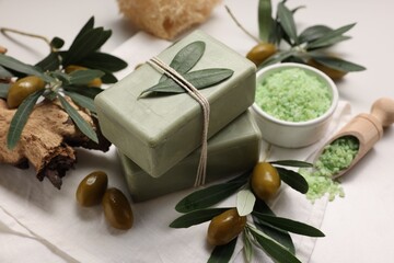 Natural soap bars, olives and sea salt on white table, closeup