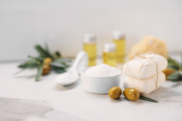 Natural soap bars, olives and sea salt on white marble table, closeup