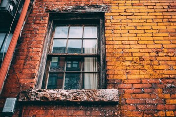 Weathered brick wall with a multipaned window showing reflections and a rugged sill